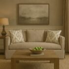 Neutral slipcovered sofa with tailored arms and damask accent pillows, featured in a traditional styled living room and studio background.
