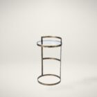 Small round accent table with an antique brass-finished frame and a clear glass top, styled beside a modern armchair in a neutral living space.