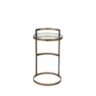 Small round accent table with an antique brass-finished frame and a clear glass top, styled beside a modern armchair in a neutral living space.