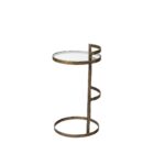 Small round accent table with an antique brass-finished frame and a clear glass top, styled beside a modern armchair in a neutral living space.