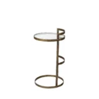 Small round accent table with an antique brass-finished frame and a clear glass top, styled beside a modern armchair in a neutral living space.