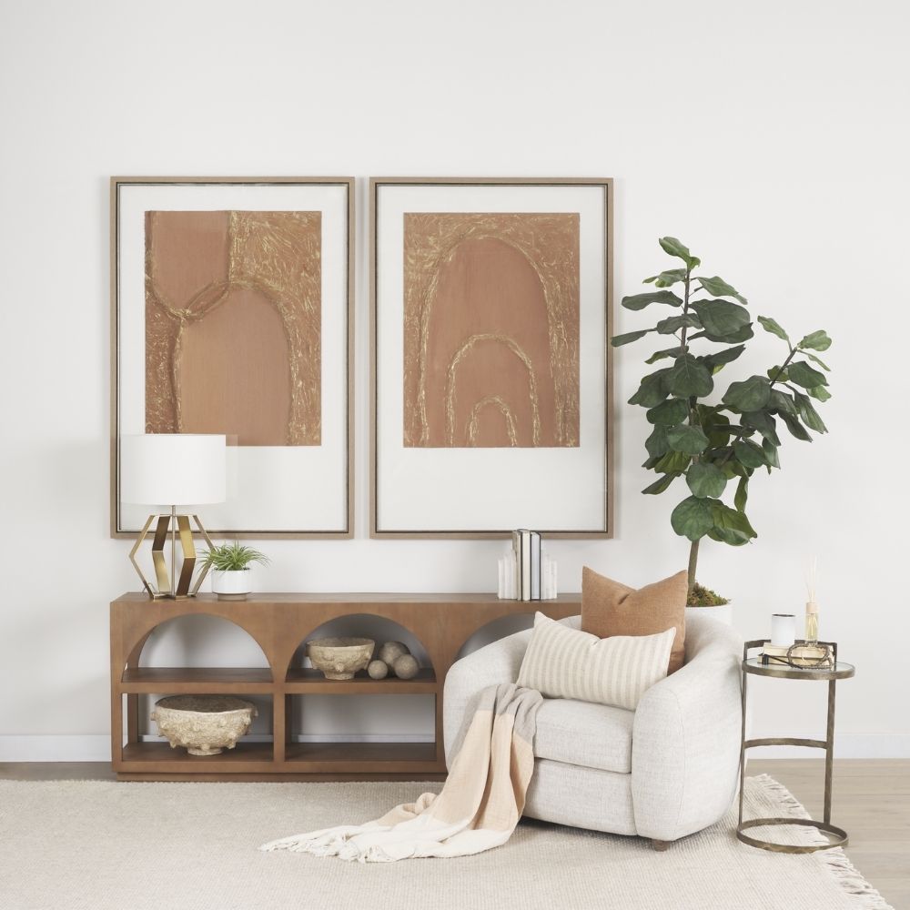 Small round accent table with an antique brass-finished frame and a clear glass top, styled beside a modern armchair in a neutral living space.