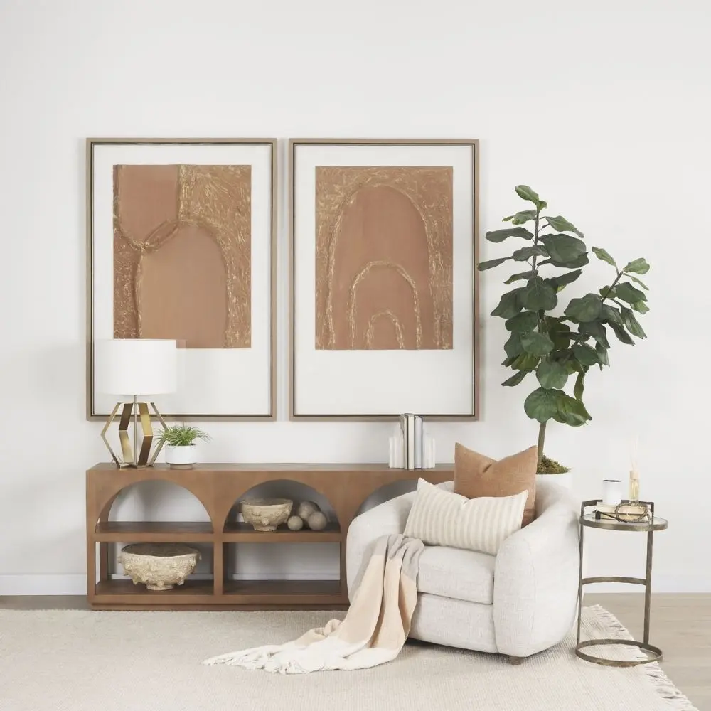 Small round accent table with an antique brass-finished frame and a clear glass top, styled beside a modern armchair in a neutral living space.