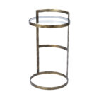 Small round accent table with an antique brass-finished frame and a clear glass top, styled beside a modern armchair in a neutral living space.