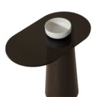 Oval black stone-topped side table with a flared wood base and brass detailing, styled next to a modern sofa in a sunlit living room.