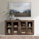 A dark wood sideboard with four framed glass doors, gold vertical handles, and interior shelving, shown with one door open and one closed.