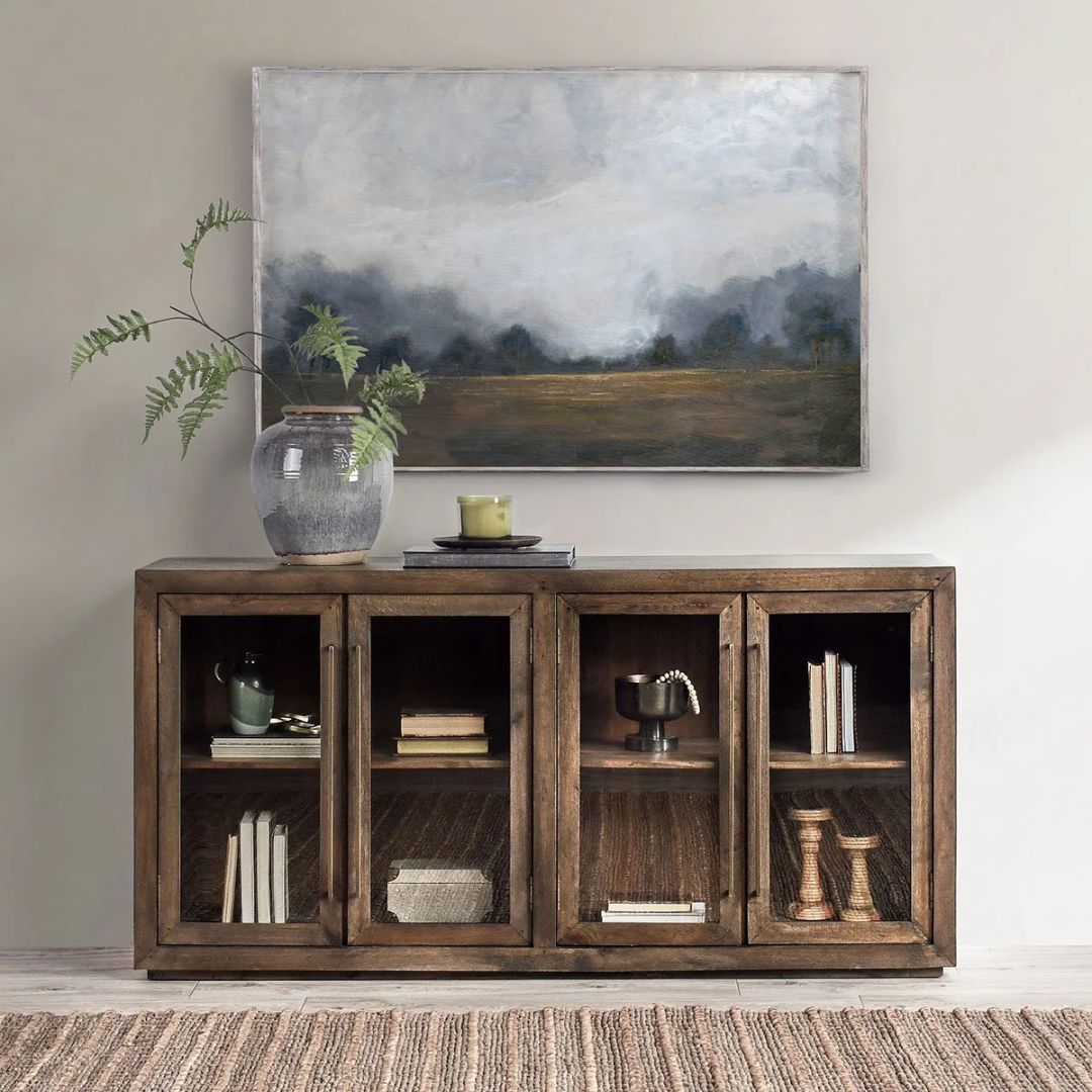 A dark wood sideboard with four framed glass doors, gold vertical handles, and interior shelving, shown with one door open and one closed.