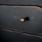 Black distressed wood two-drawer nightstand with tapered legs and rounded drawer fronts.