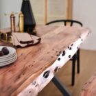 Rectangular live-edge wood dining table with a natural finish and matte black metal cross-frame legs.