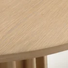 A round natural wood dining table with a sculptural, fluted pedestal base, styled on a soft neutral background.