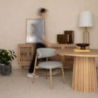 A round natural wood dining table with a sculptural, fluted pedestal base, styled on a soft neutral background.