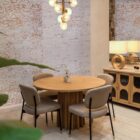 A round natural wood dining table with a sculptural, fluted pedestal base, styled on a soft neutral background.