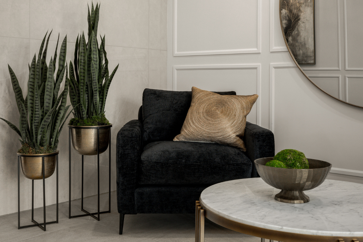 Stylish corner vignette featuring a black velvet armchair and two faux snake plants in metallic planters.