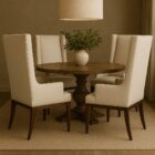 A high-back, upholstered dining chair with wingback arms, straight profile, and a dark wood leg frame.