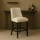 Stool in Cream Fabric with Black Wood Legs, Highlighting Nailhead Trim.