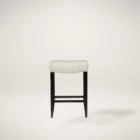 A backless upholstered saddle stool with cream fabric seat, dark espresso wood frame, and footrest support.