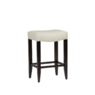 A backless upholstered saddle stool with cream fabric seat, dark espresso wood frame, and footrest support.
