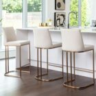 A modern upholstered counter stool with a curved brass-finished metal base and light neutral fabric seat and back.