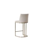A modern upholstered counter stool with a curved brass-finished metal base and light neutral fabric seat and back.