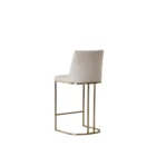 A modern upholstered counter stool with a curved brass-finished metal base and light neutral fabric seat and back.