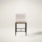 A modern upholstered counter stool with a soft cream fabric seat and backrest, wooden trim, and sleek black metal legs.