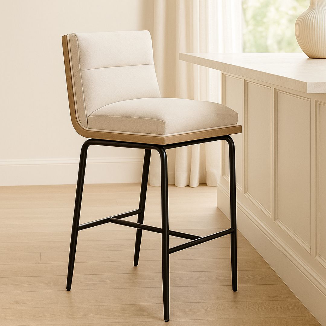 A modern upholstered counter stool with a soft cream fabric seat and backrest, wooden trim, and sleek black metal legs.