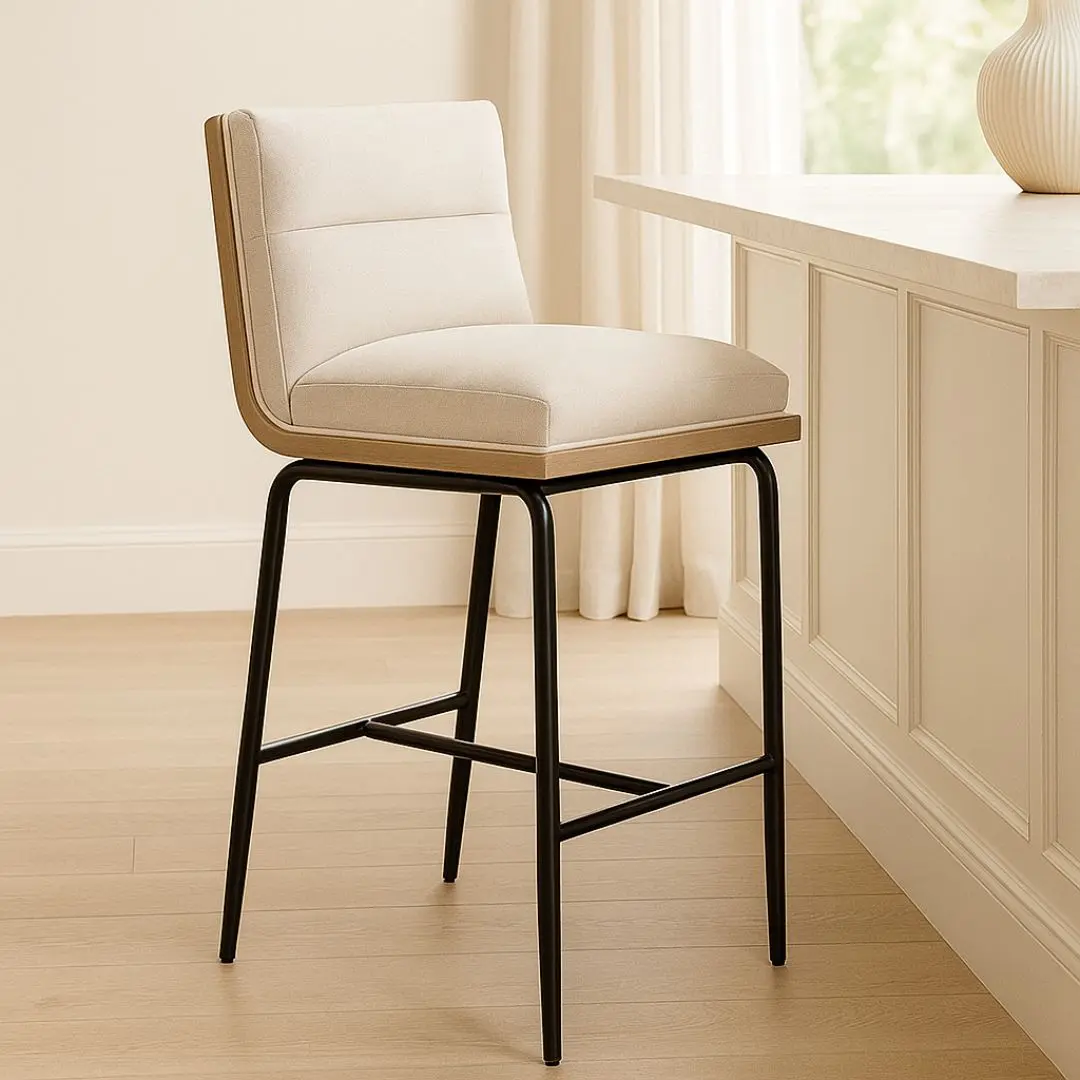 A modern upholstered counter stool with a soft cream fabric seat and backrest, wooden trim, and sleek black metal legs.
