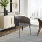 Modern barrel-back dining armchair with charcoal grey fabric seat, faux leather exterior, black tapered legs, and brass metal caps.