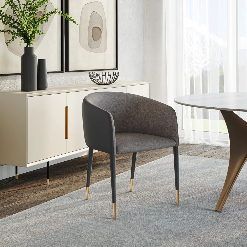 Modern barrel-back dining armchair with charcoal grey fabric seat, faux leather exterior, black tapered legs, and brass metal caps.
