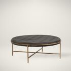 Round tufted ottoman with charcoal black upholstery and slender antique brass base frame.