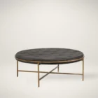 Round tufted ottoman with charcoal black upholstery and slender antique brass base frame.