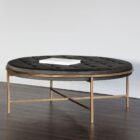 Round tufted ottoman with charcoal black upholstery and slender antique brass base frame.