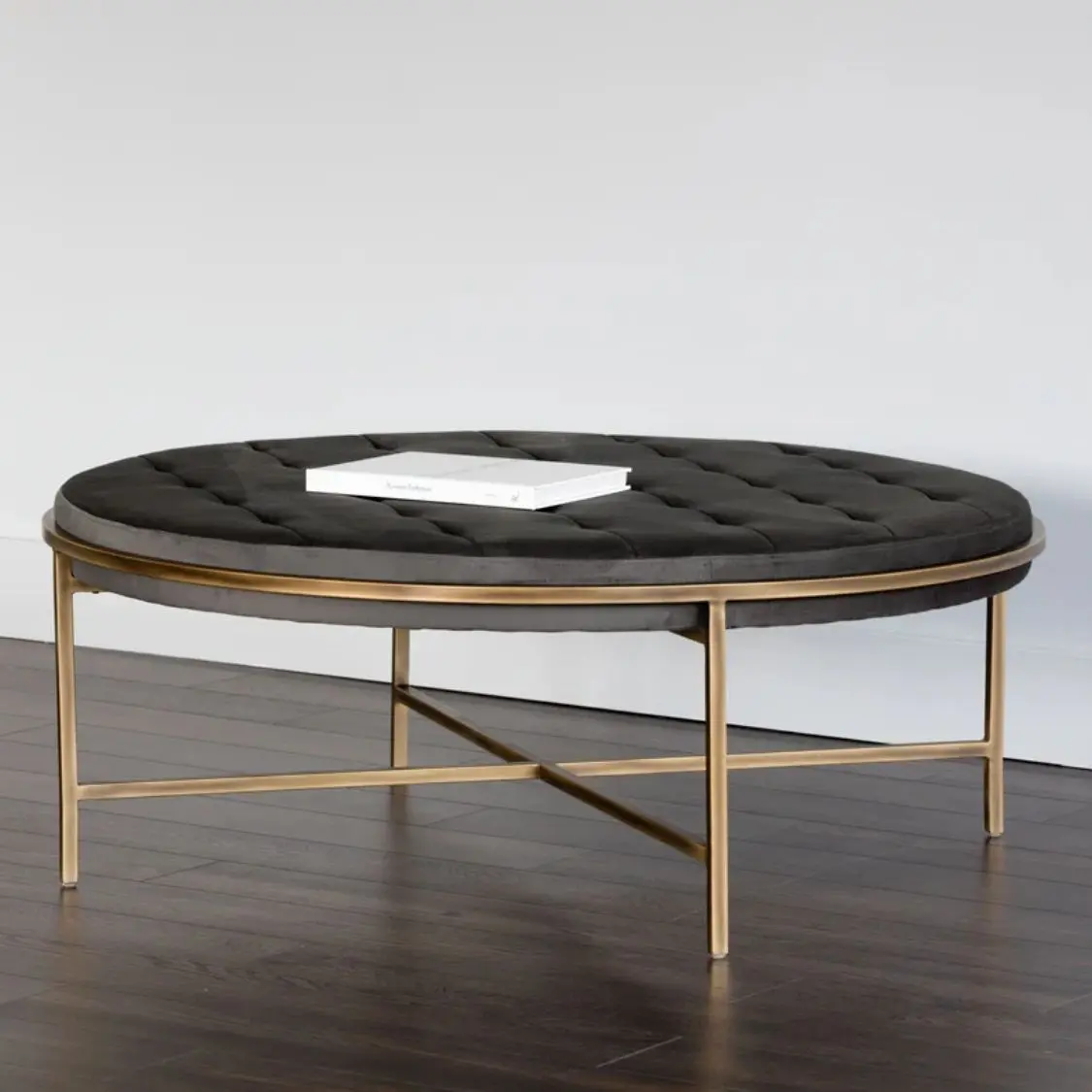 Round tufted ottoman with charcoal black upholstery and slender antique brass base frame.