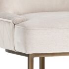 Elegant stool with soft beige upholstered seat and curved gold metal base.
