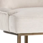 Elegant stool with soft beige upholstered seat and curved gold metal base.