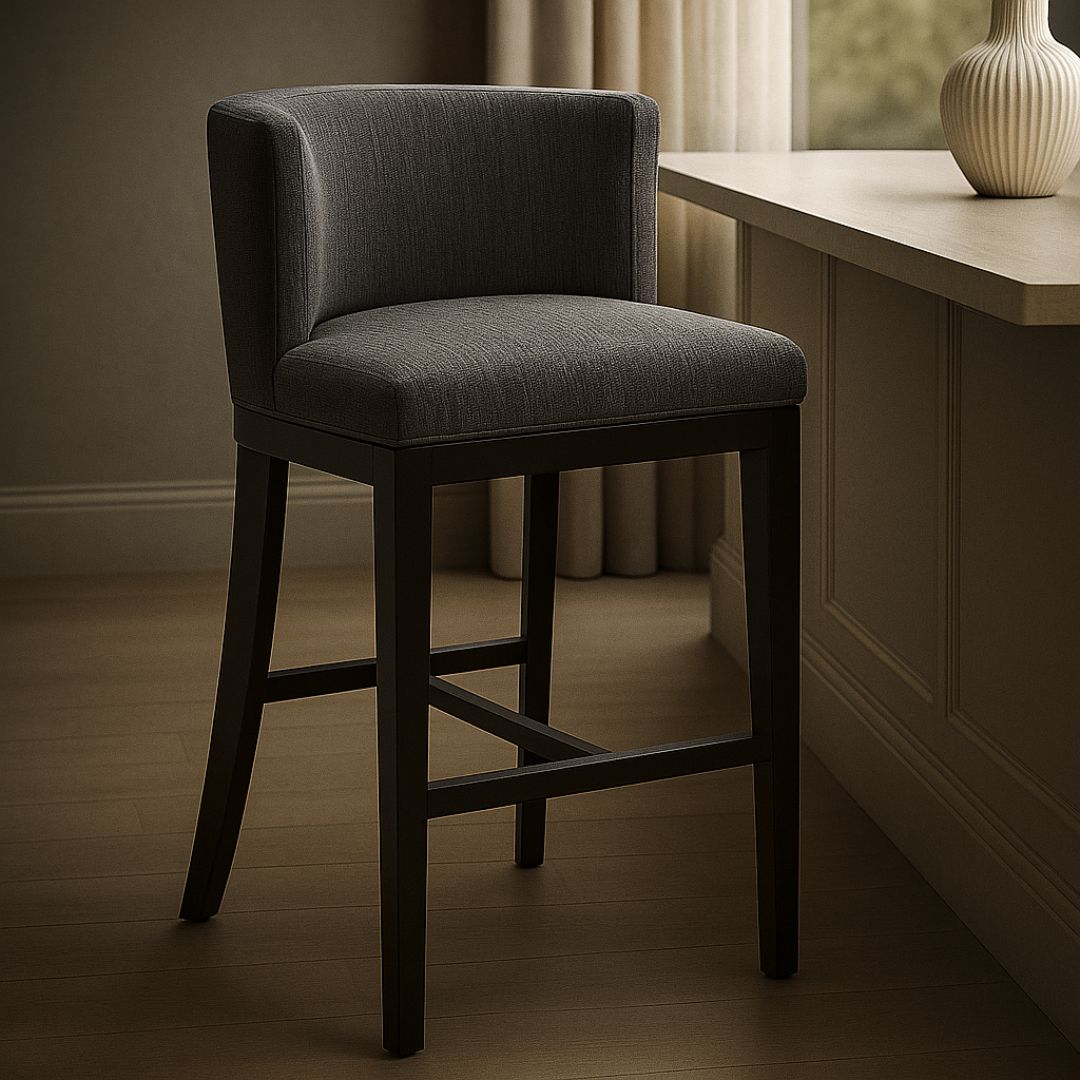 Dark grey upholstered barstool with low backrest and black wooden legs, styled beside a light wood countertop in a neutral-toned interior.