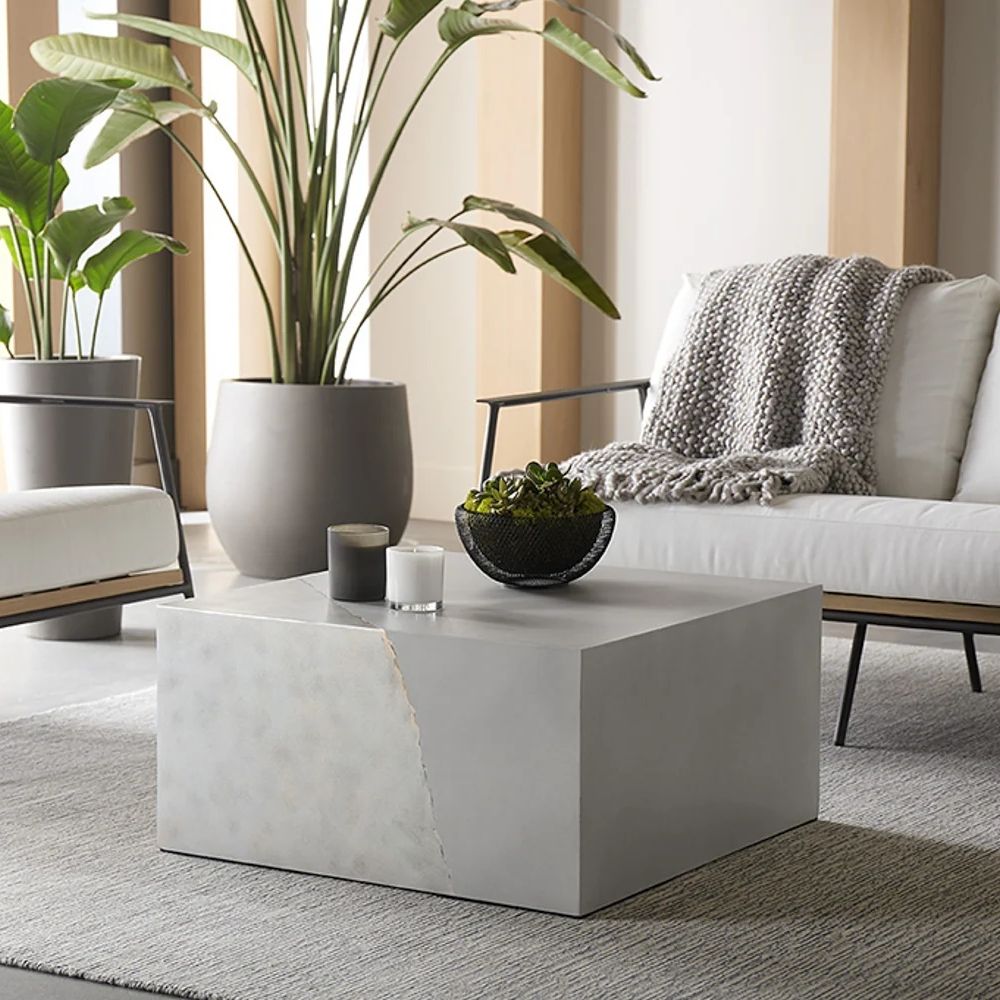 Square concrete coffee table with angular crack-inspired detail and softly weathered stone texture.