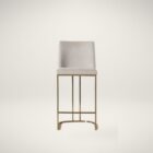 A modern upholstered counter stool with a curved brass-finished metal base and light neutral fabric seat and back.