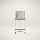 A modern upholstered counter stool with a curved brass-finished metal base and light neutral fabric seat and back.