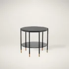 Round modern end table with black textured top, slim black legs, lower shelf, and brass-capped feet.