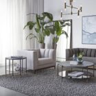 Round modern end table with black textured top, slim black legs, lower shelf, and brass-capped feet.