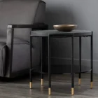 Round modern end table with black textured top, slim black legs, lower shelf, and brass-capped feet.