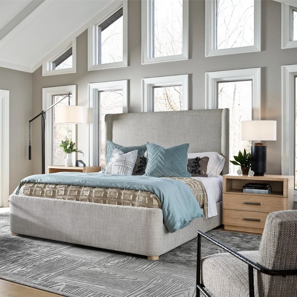 Upholstered bed with a high winged headboard in textured neutral fabric, rounded corners, and low wood feet, shown in both studio and lifestyle settings.