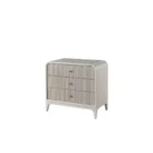 A modern three-drawer nightstand with soft, rounded corners and reeded drawer fronts, finished in a light neutral tone with gold hardware, styled beside a contemporary upholstered bed.