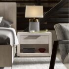A modern Huston Nightstand featuring a sleek open-frame design with a single drawer and lower shelf in a light wood finish, styled beside a contemporary bed.