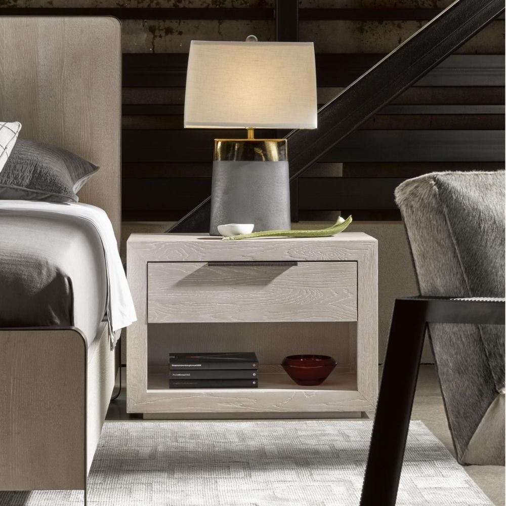 A modern Huston Nightstand featuring a sleek open-frame design with a single drawer and lower shelf in a light wood finish, styled beside a contemporary bed.