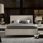 A modern Huston Nightstand featuring a sleek open-frame design with a single drawer and lower shelf in a light wood finish, styled beside a contemporary bed.