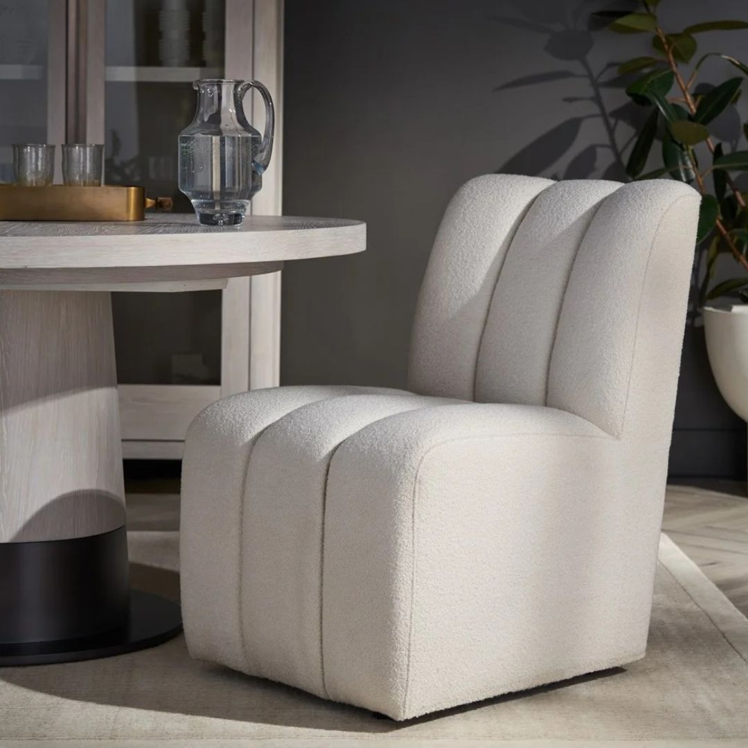 A modern armless side chair in soft ivory bouclé with deep vertical channelling on the seat and back, featuring a fully upholstered silhouette.