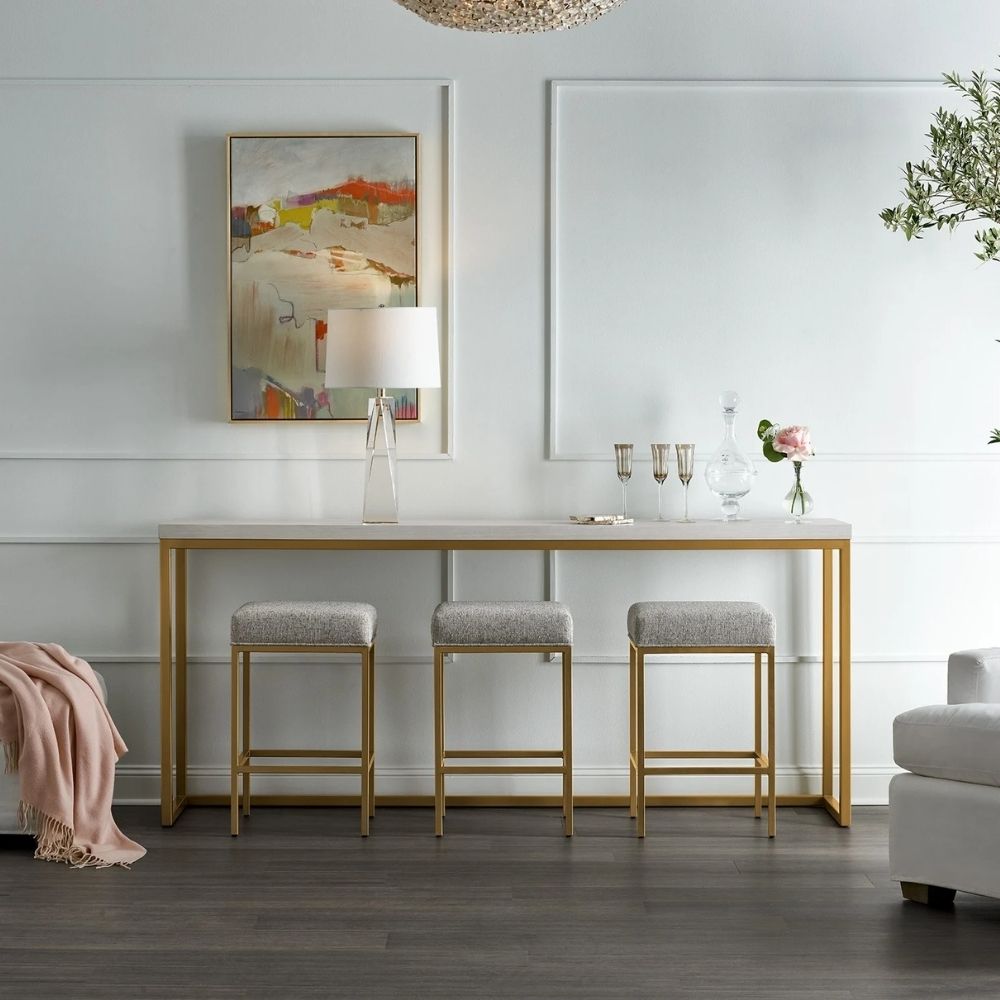 Elegant console table with a white top and brushed gold frame, paired with three coordinating upholstered stools.