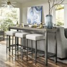 Industrial-style console table with a natural wood top, black metal frame, and three upholstered stools in ivory fabric.